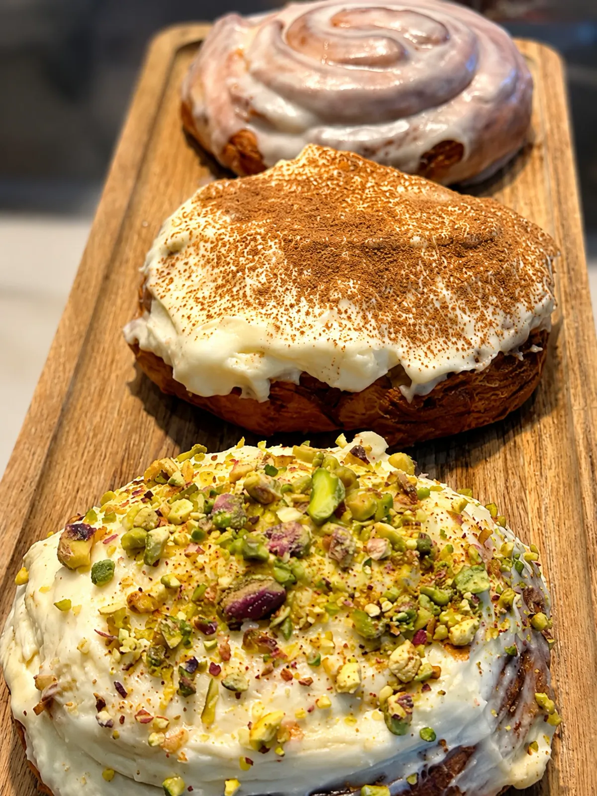 Tres cinnamon rolls apilados: glaseado, frosting con canela y pistacho.