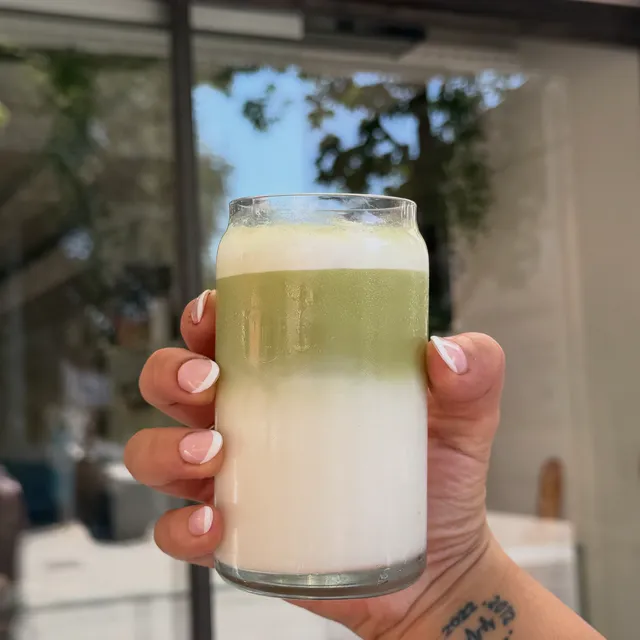Vaso de matcha con leche en dos capas, en la mano.