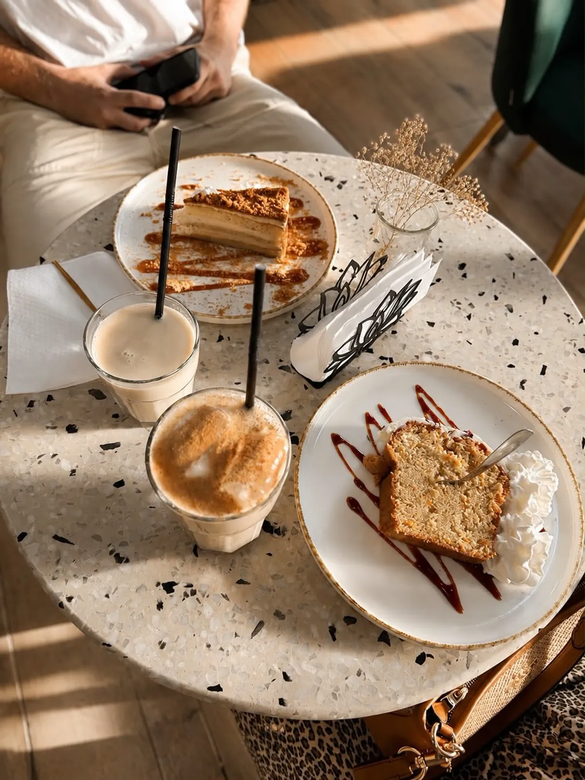 Una porción de carrot cake y otra de lotus cake con dos bebidas frías, sobre mesa de terrazo.